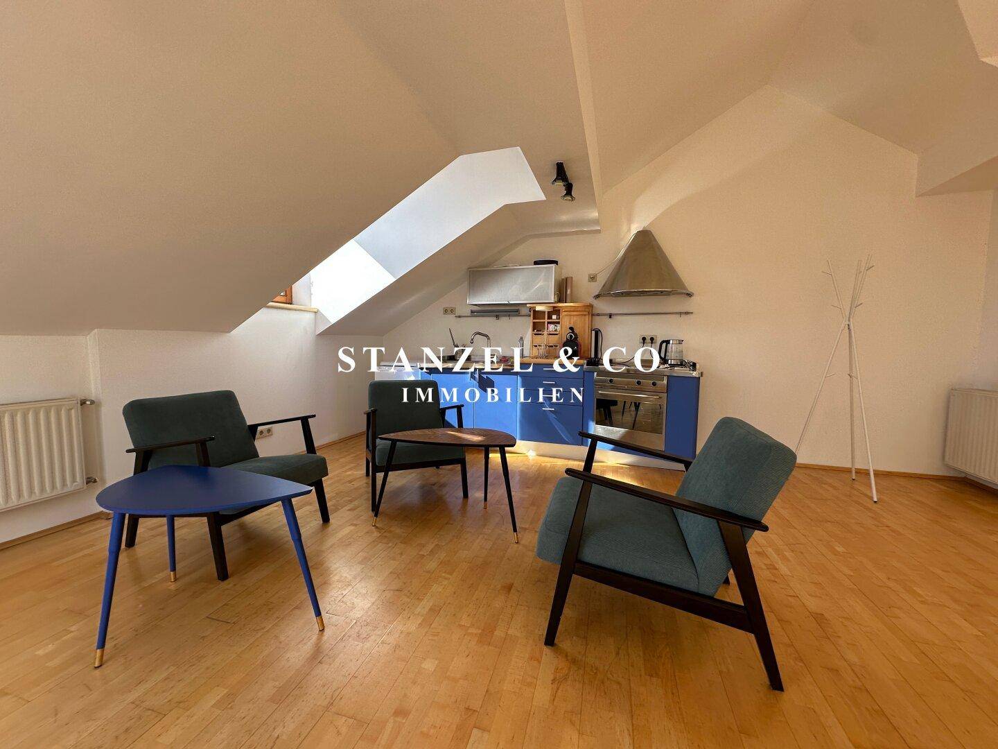 Gemütliche Sitzecke und Küchenzeile im Dachgeschoss mit schrägen Decken und einem Dachfenster für zusätzliches Licht.