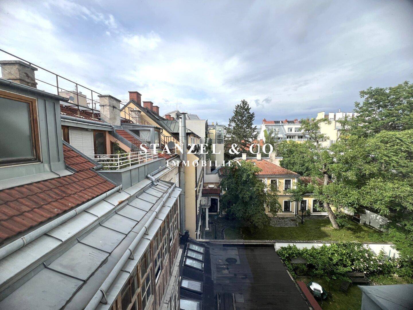Ausblick über die Dächer der Stadt mit viel Grün und Bäumen im Hintergrund.