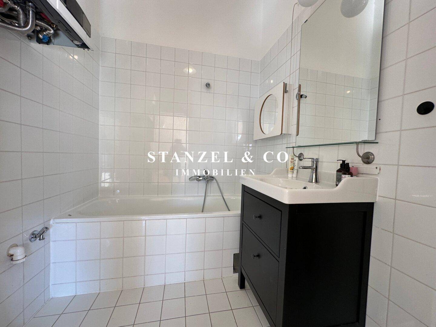Modernes Badezimmer mit weißen Fliesen, einer Badewanne und einem Waschtisch mit Spiegel.