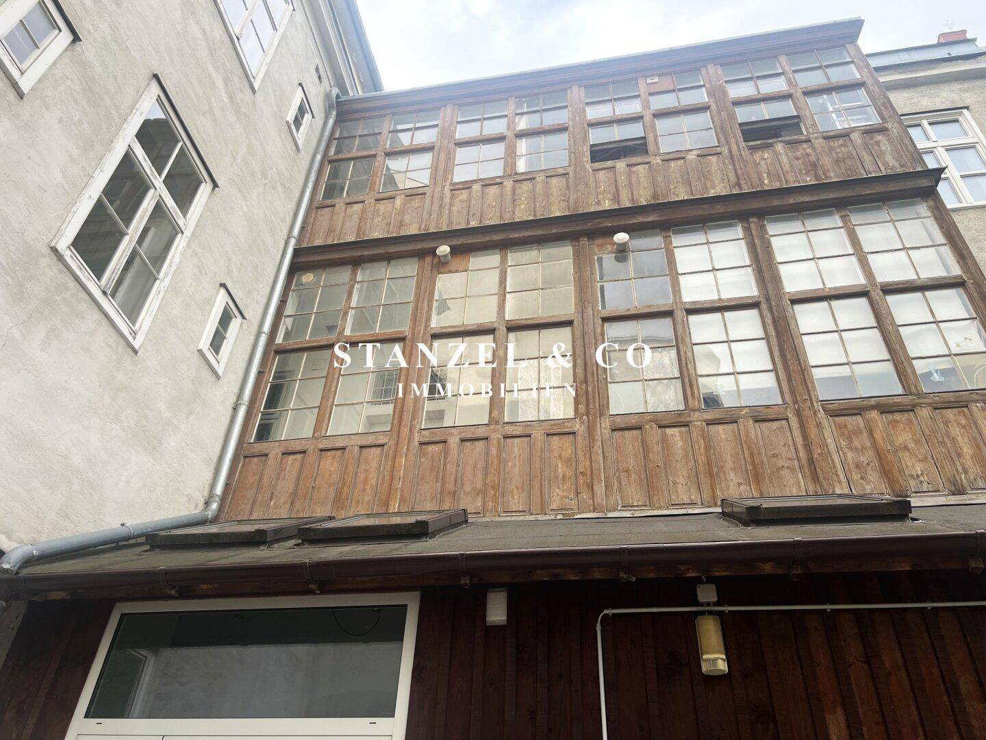 Alte Holzfassade eines Gebäudes mit vielen Fenstern und verglasten Anbauten.