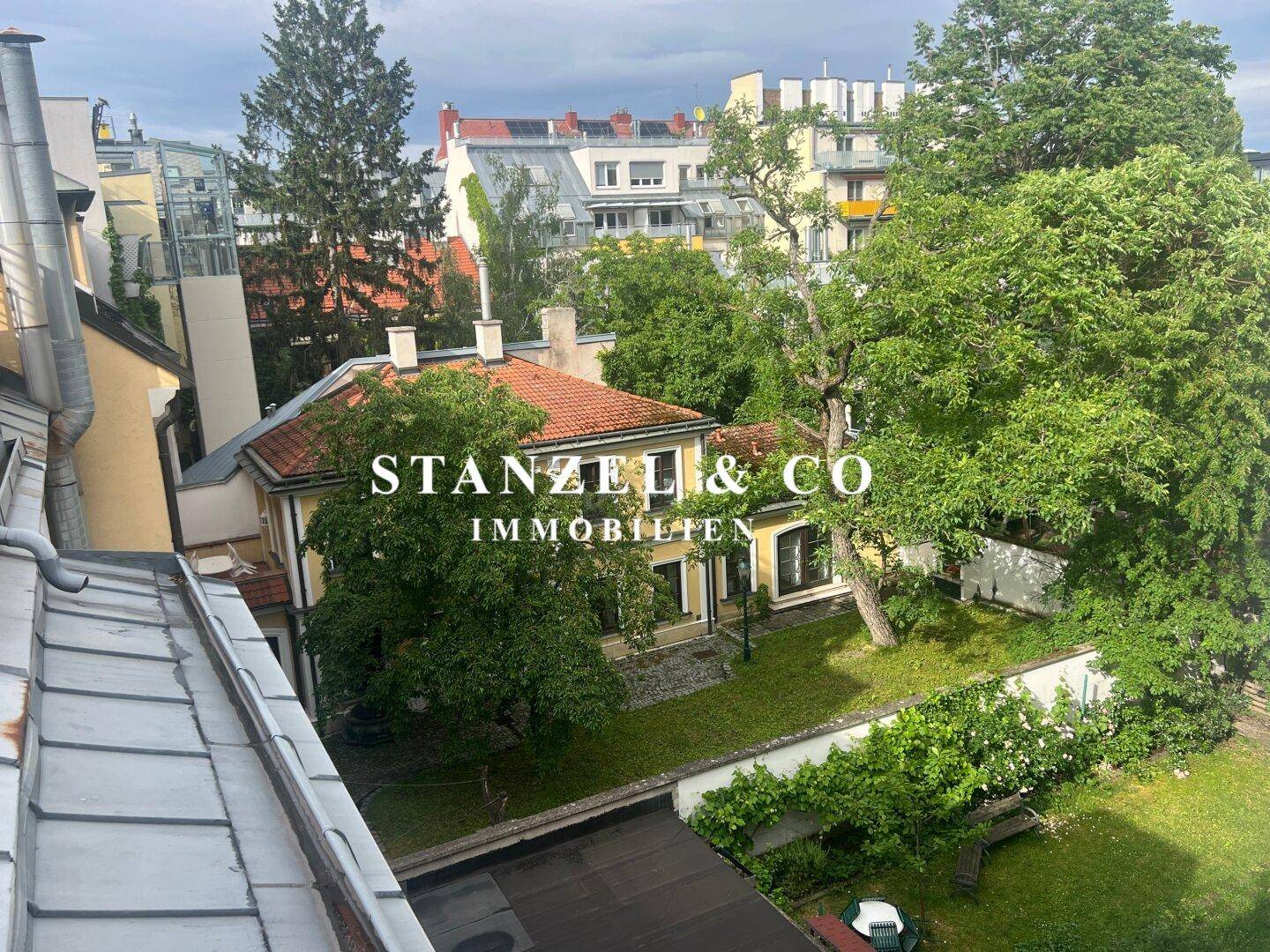 Luftaufnahme eines Hauses mit großem, gepflegtem Garten und altem Baumbestand in städtischer Umgebung.