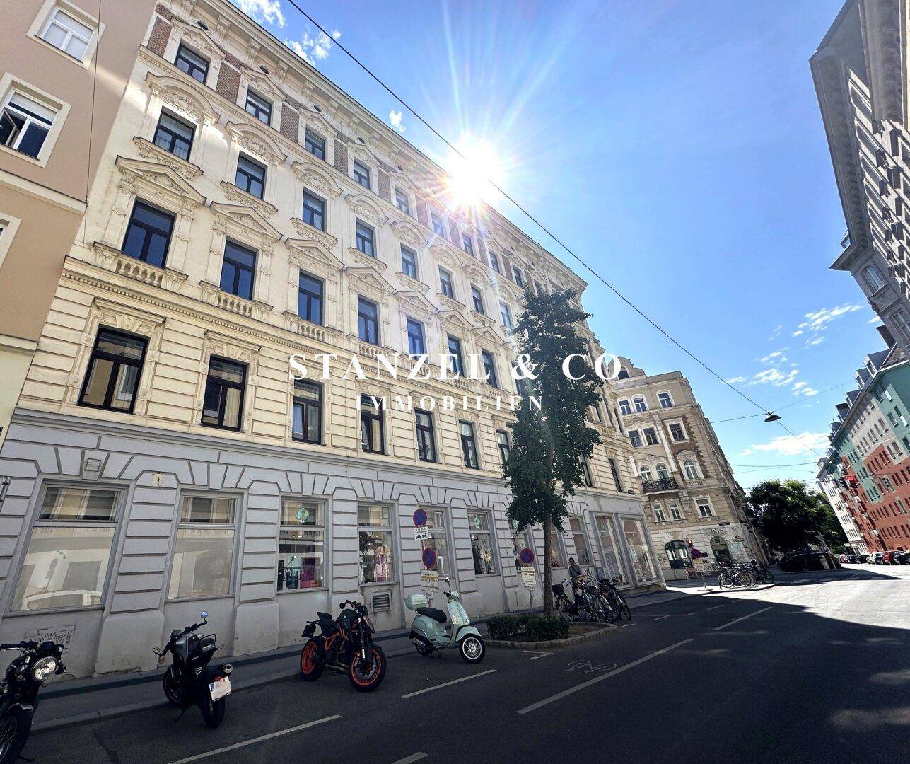 Sonnenbeschienene Fassade eines Altbaus mit vielen Fenstern und Geschäften im Erdgeschoss.