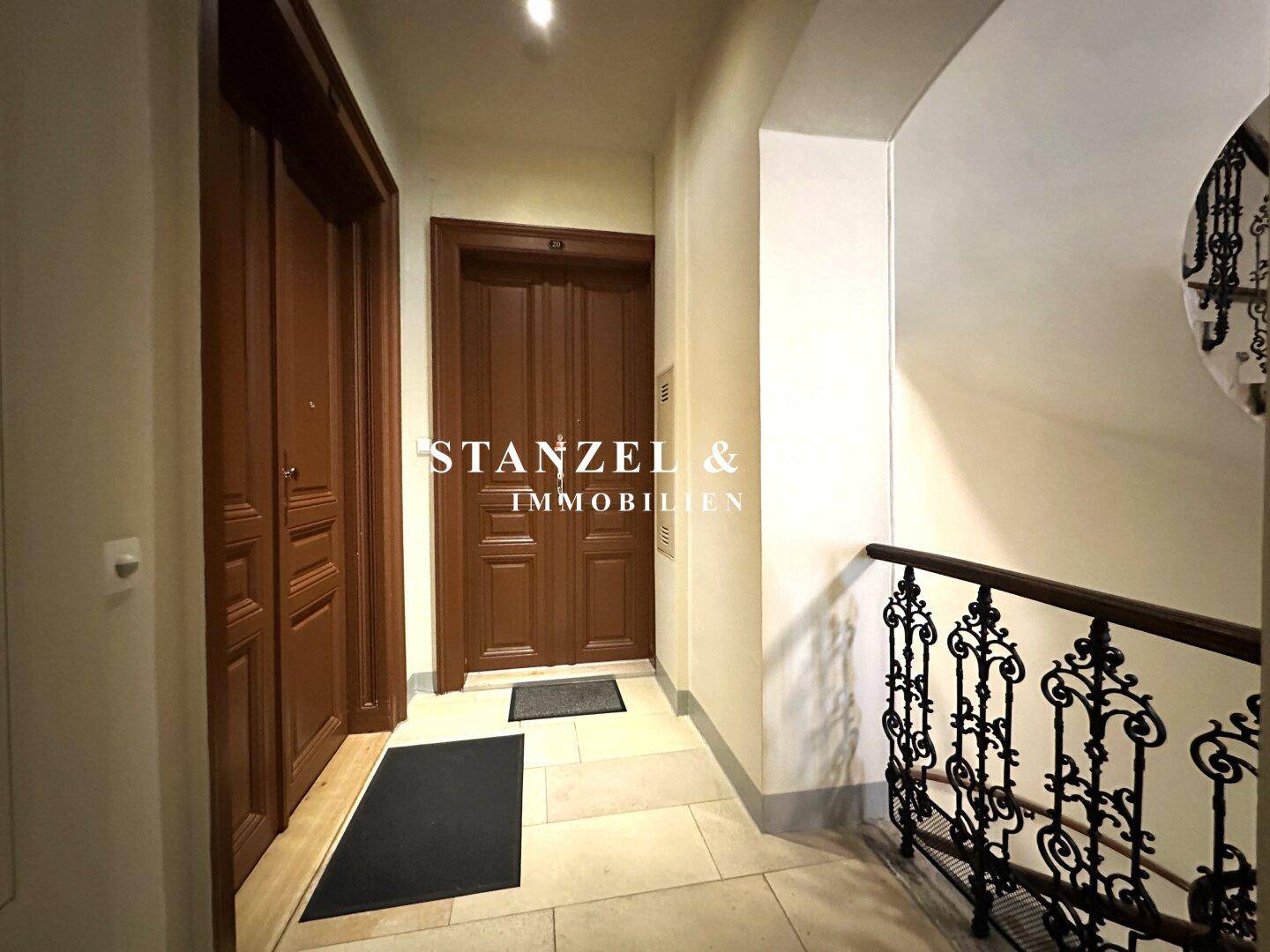 Heller Flur mit zwei Holztüren und Zugang zum eleganten Treppenhaus.