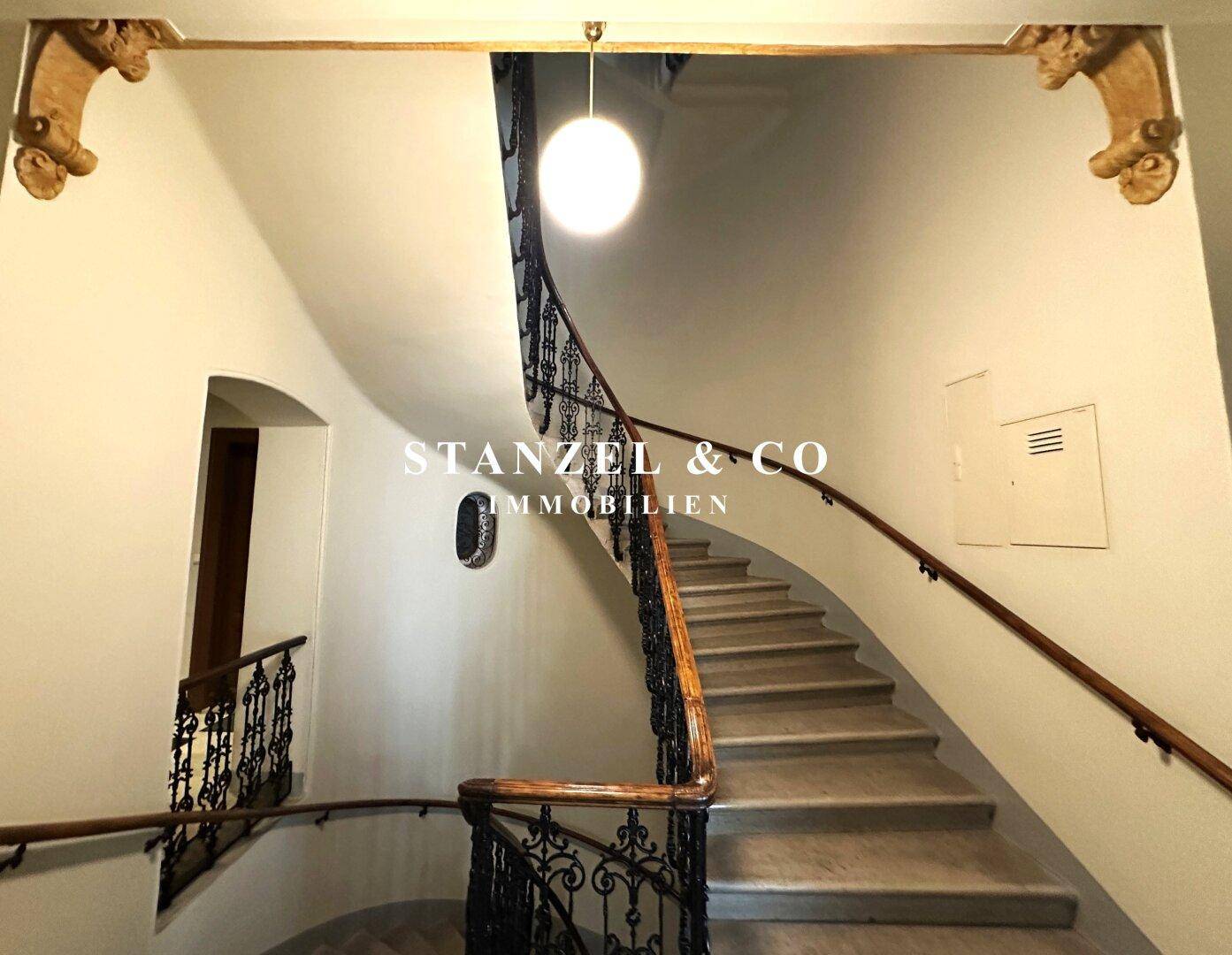 Elegante Wendeltreppe mit schmiedeeisernem Geländer und dekorativer Deckenleuchte.