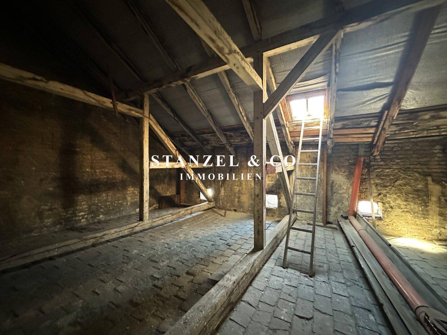 Unausgebauter Dachboden mit Holzbalken, Dachfenster und einer Leiter, ideal für Ausbau.