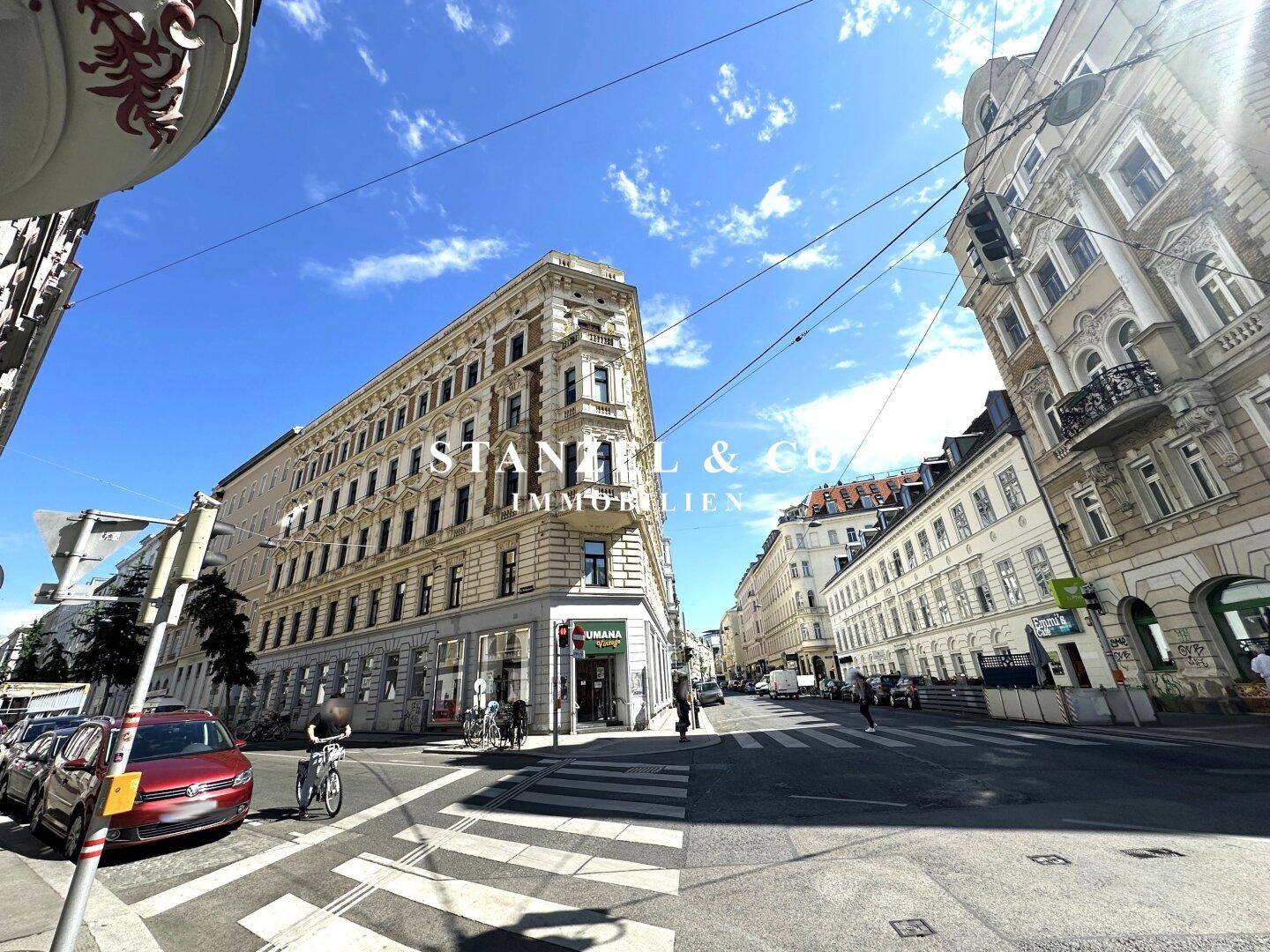 Historisches Eckgebäude in einer belebten Stadtstraße unter blauem Himmel.