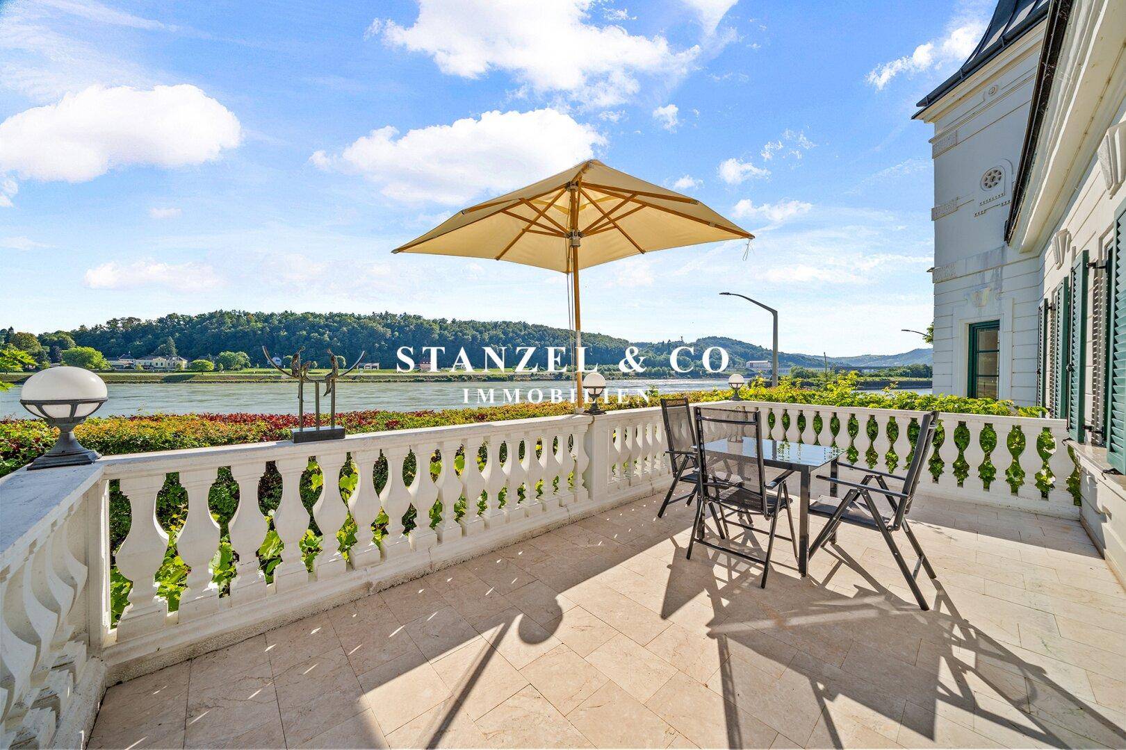 Elegante Terrasse mit Balustrade, Sitzgelegenheiten und weitem Blick auf den Fluss.