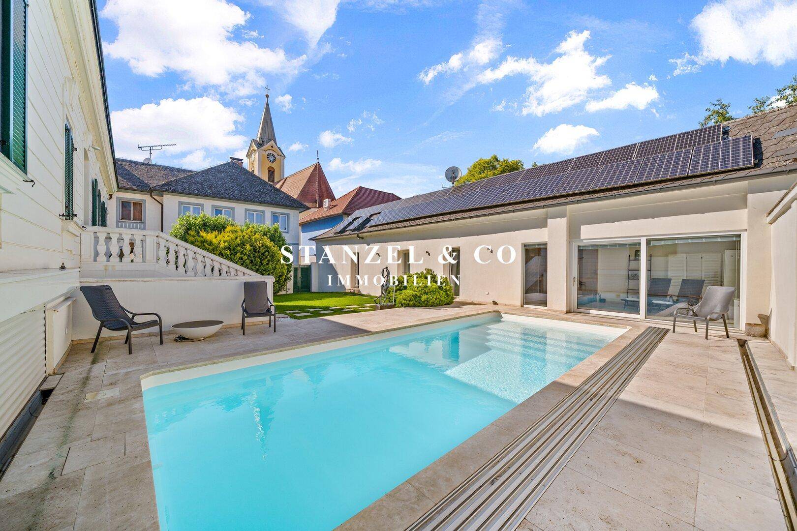 Außenansicht des Hauses mit Poolbereich, Rasenfläche und Photovoltaikanlage auf dem Dach.