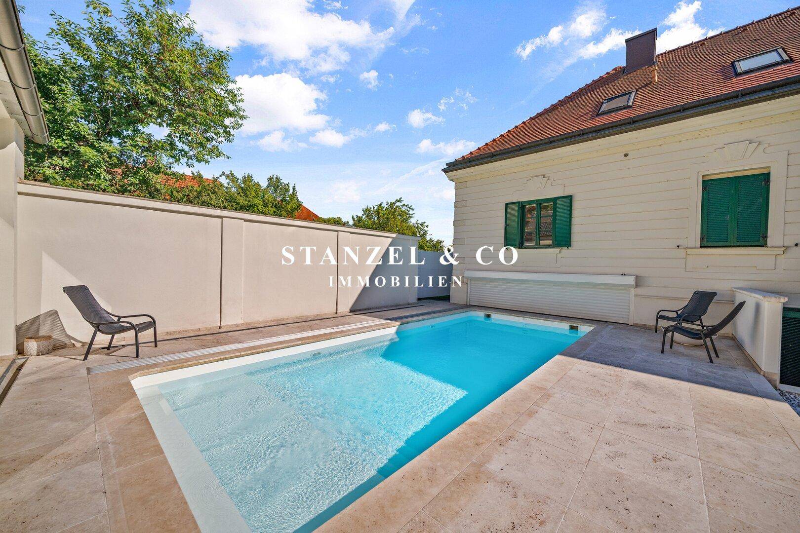 Privater Poolbereich mit heller Steinumrandung und Liegestühlen, ideal zum Entspannen.