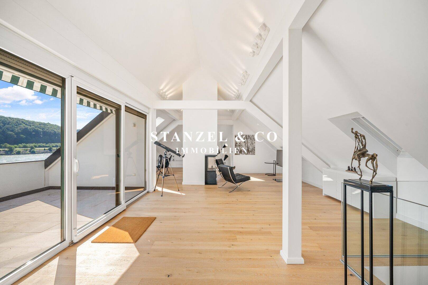 Offener Wohnbereich im Dachgeschoss mit Holzboden, Kamin und Zugang zur Dachterrasse.