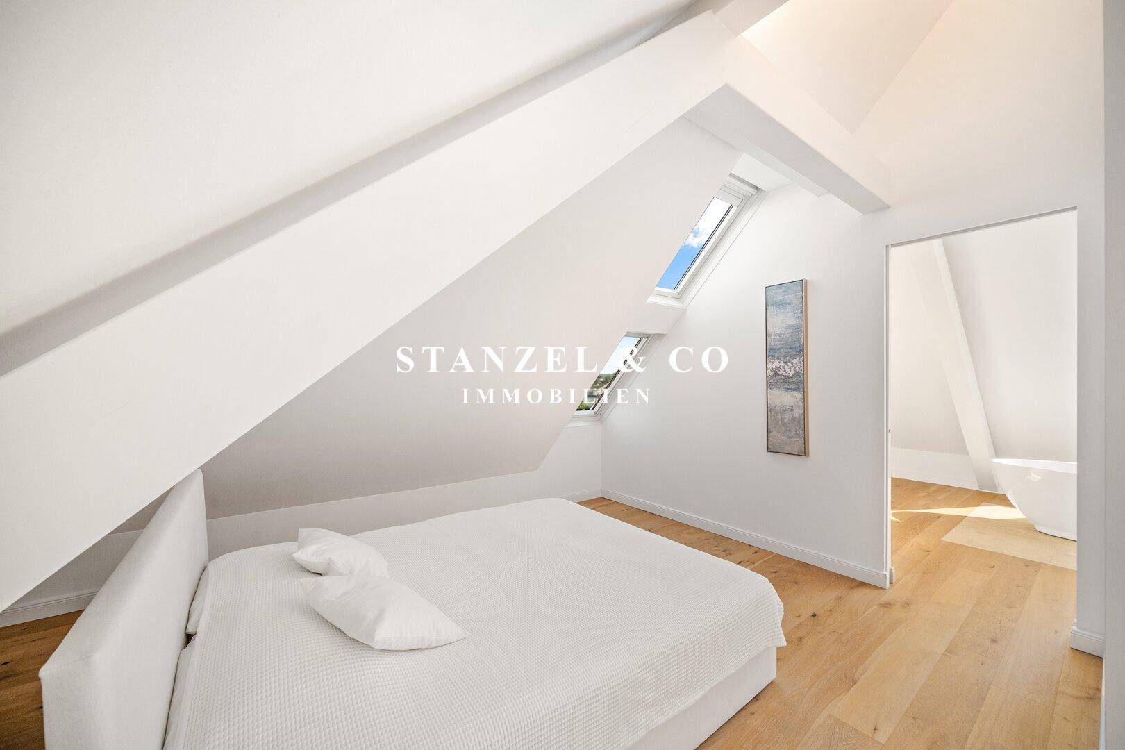 Helles Schlafzimmer im Dachgeschoss mit Holzboden, Dachfenstern und minimalistischer Einrichtung.