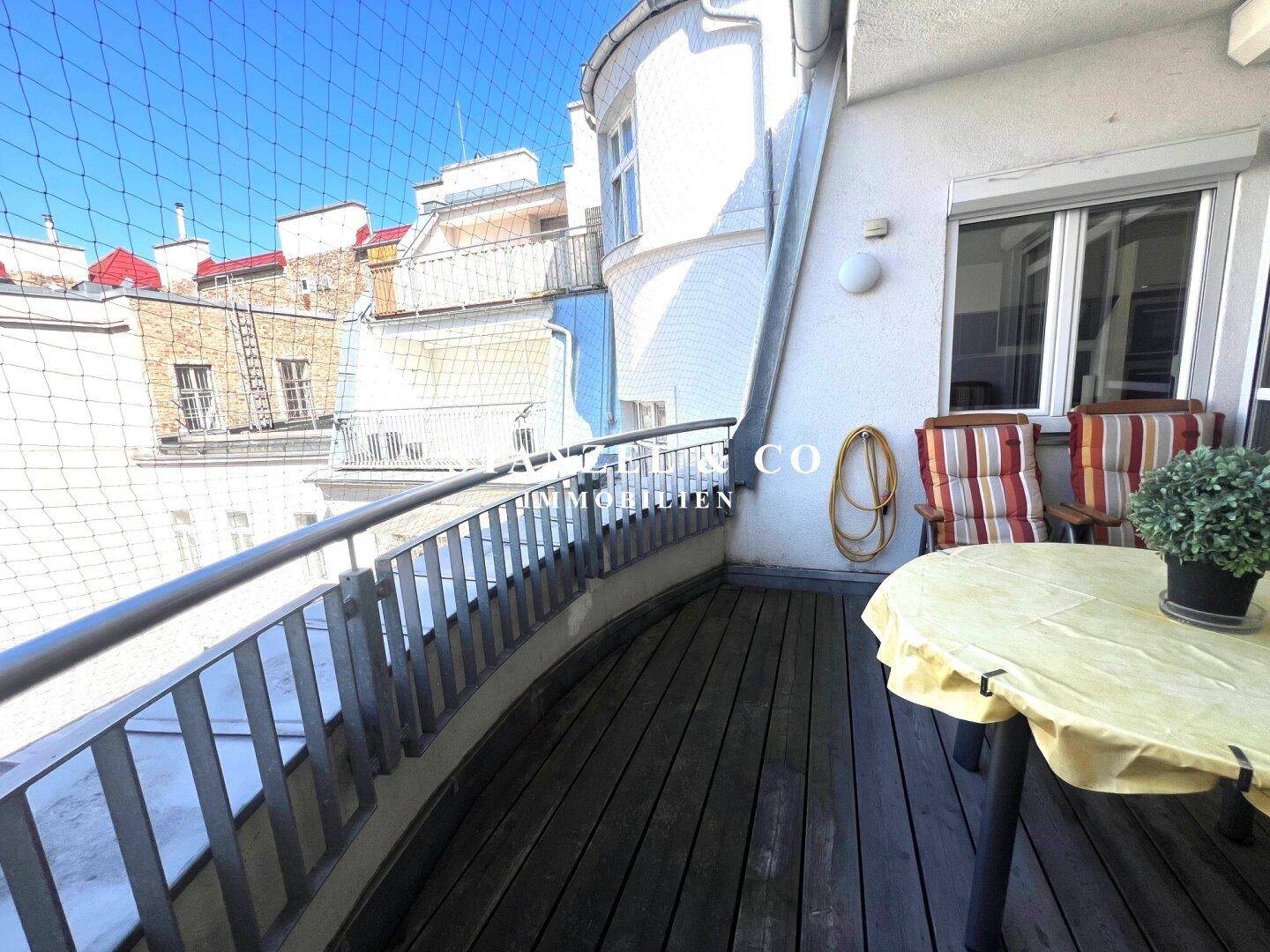 Geräumiger Balkon mit Sitzgelegenheiten und Blick auf die Dächer der Stadt.