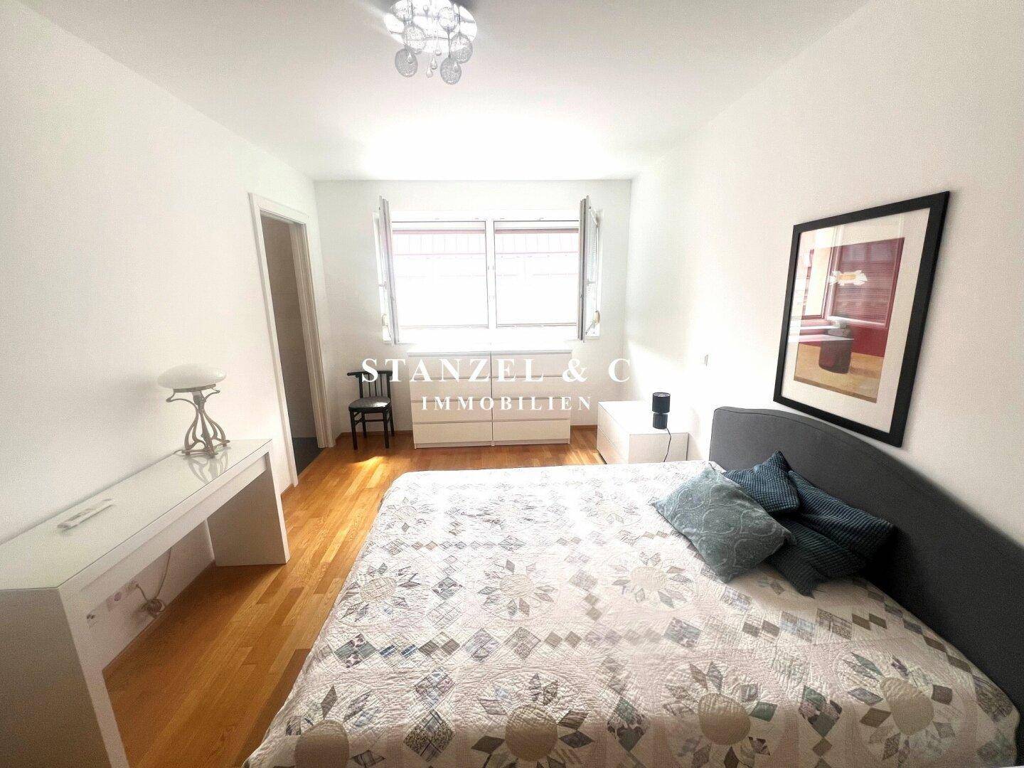 Helles Schlafzimmer mit Holzboden und großen Fenstern, die viel Tageslicht hereinlassen.