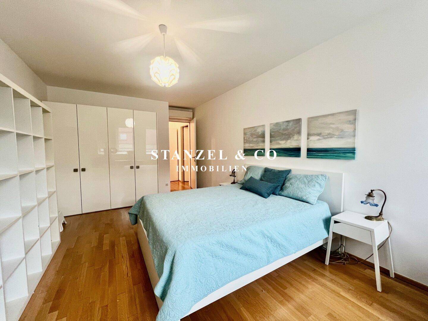 Helles Schlafzimmer mit Holzboden, weißen Einbauschränken und einem großen Bett.
