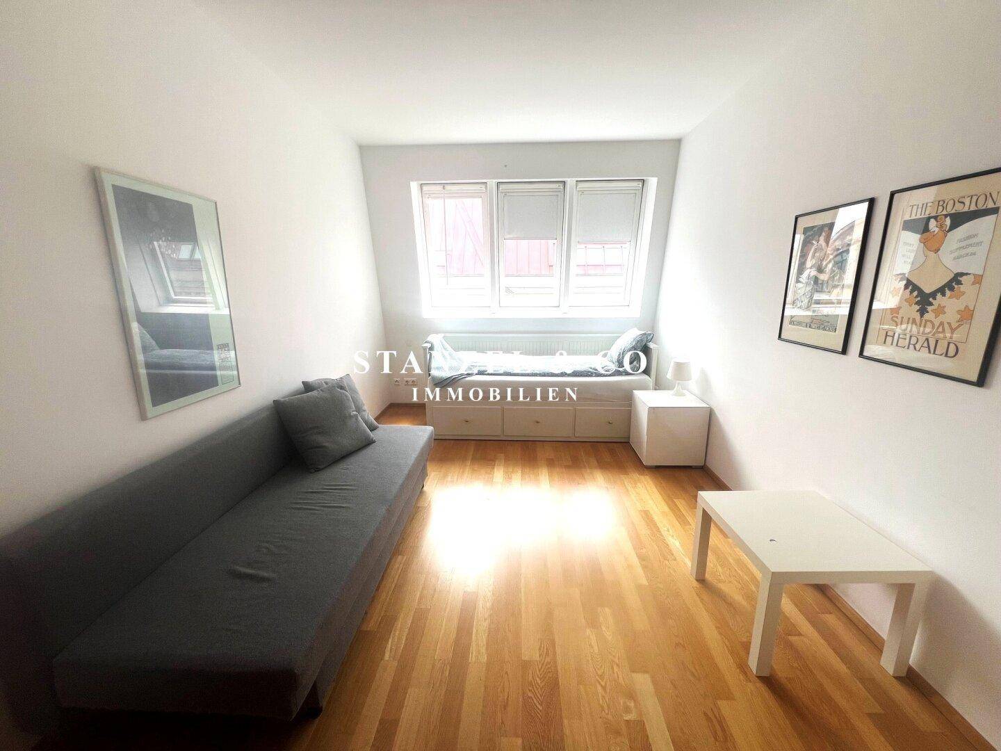 Gemütliches Zimmer mit Holzboden, Tagesbett unter dem Fenster und einem Sofa.