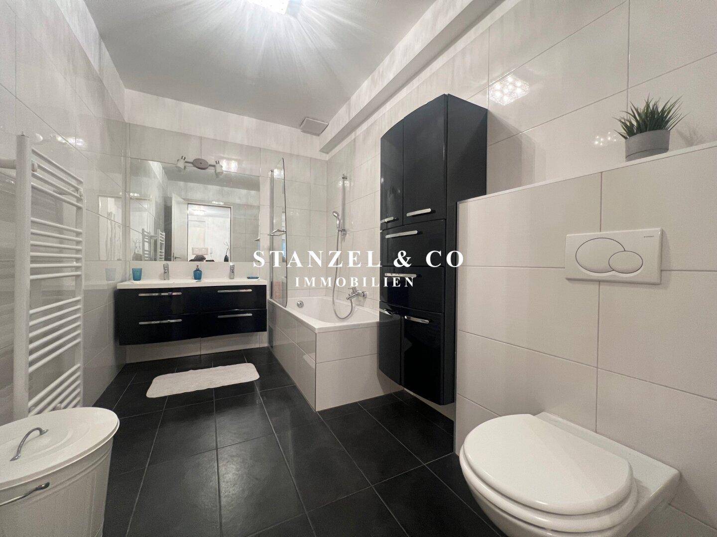 Modernes Badezimmer mit Badewanne, Doppelwaschbecken und schwarz-weißen Fliesen.