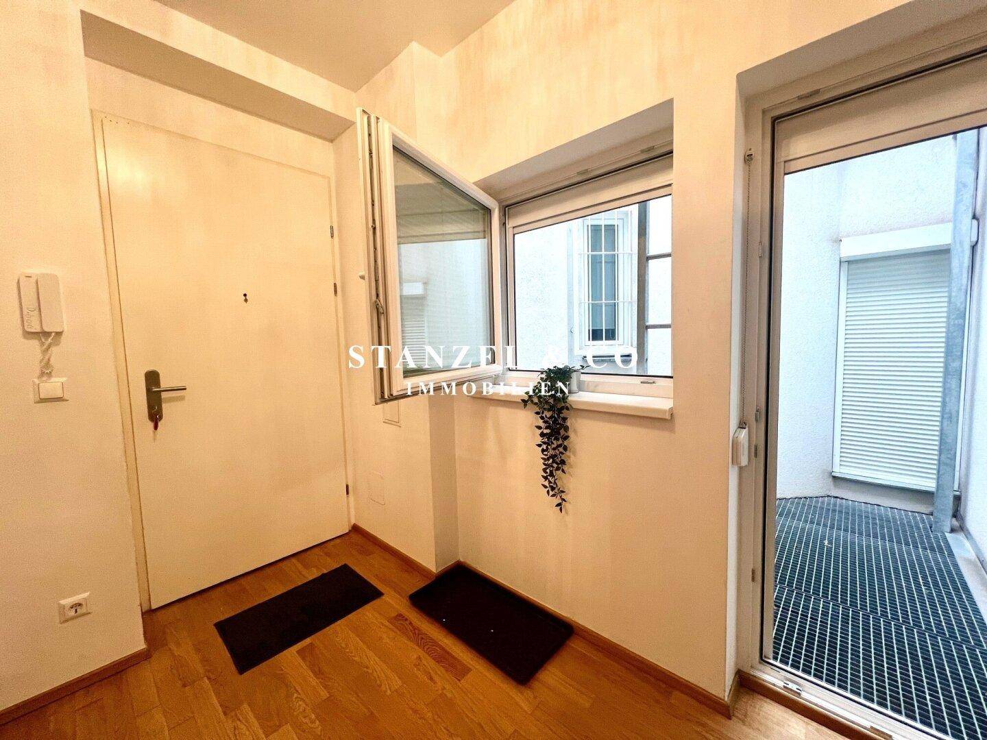 Eingangsbereich mit Holzboden, Haustür und Zugang zu einem kleinen Innenhof.