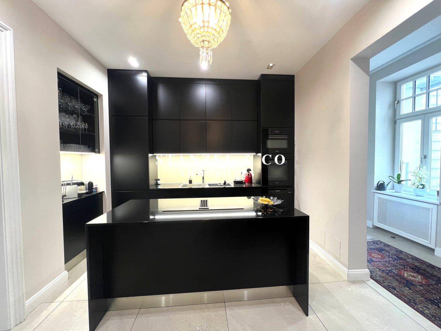 Elegante schwarze Küche mit minimalistischem Design, Kochinsel und hochwertigen Einbaugeräten.