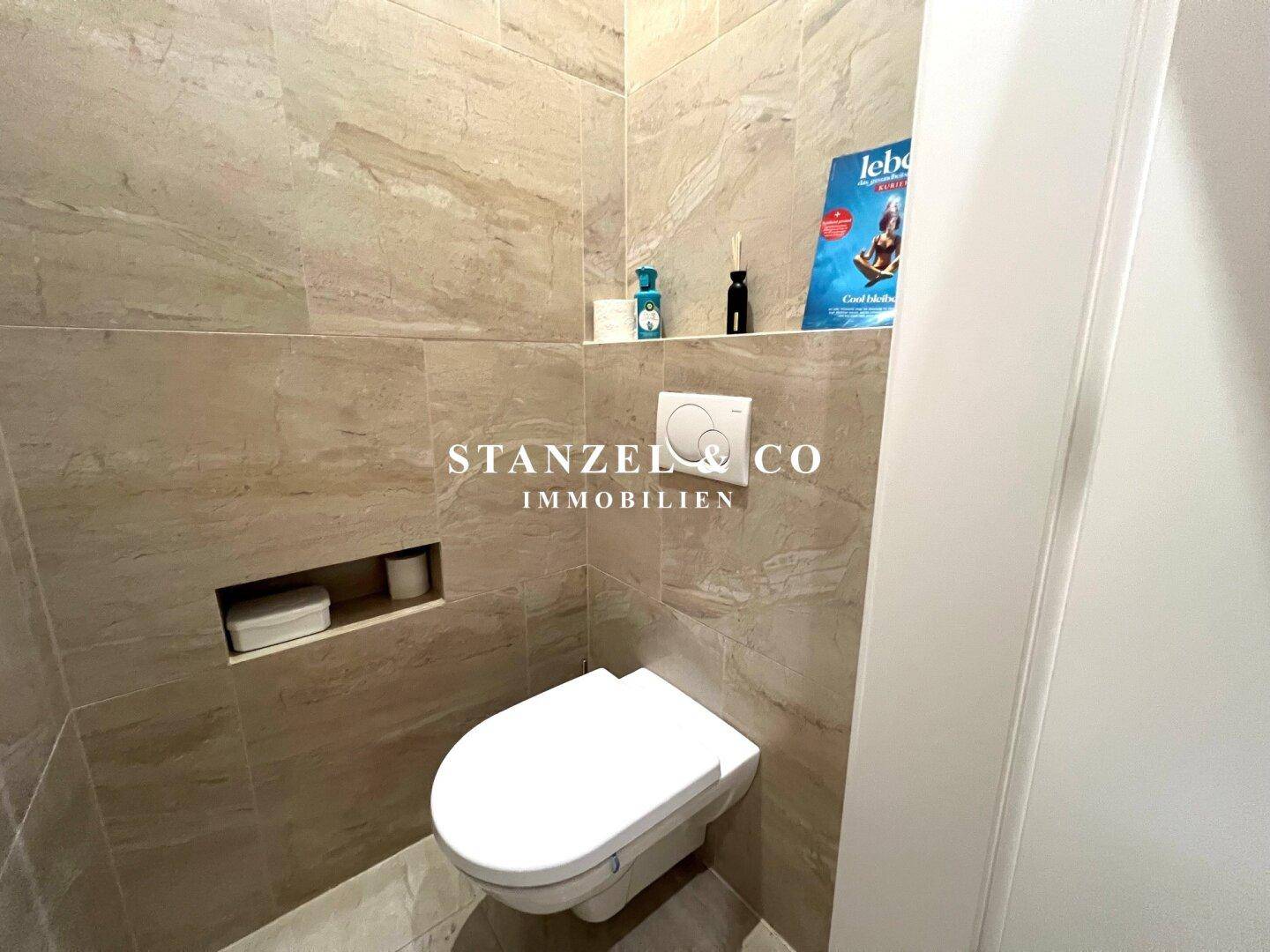 Modernes Gäste-WC mit beigefarbenen Fliesen und wandhängendem WC in zeitgemäßem Design.