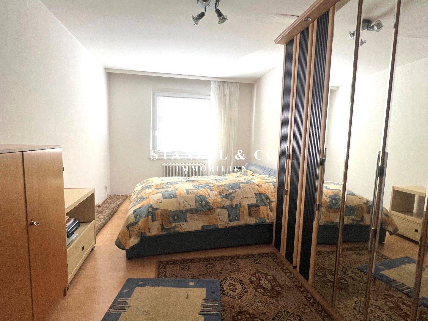 Schlafzimmer mit Doppelbett, Teppich und großem Spiegelschrank.