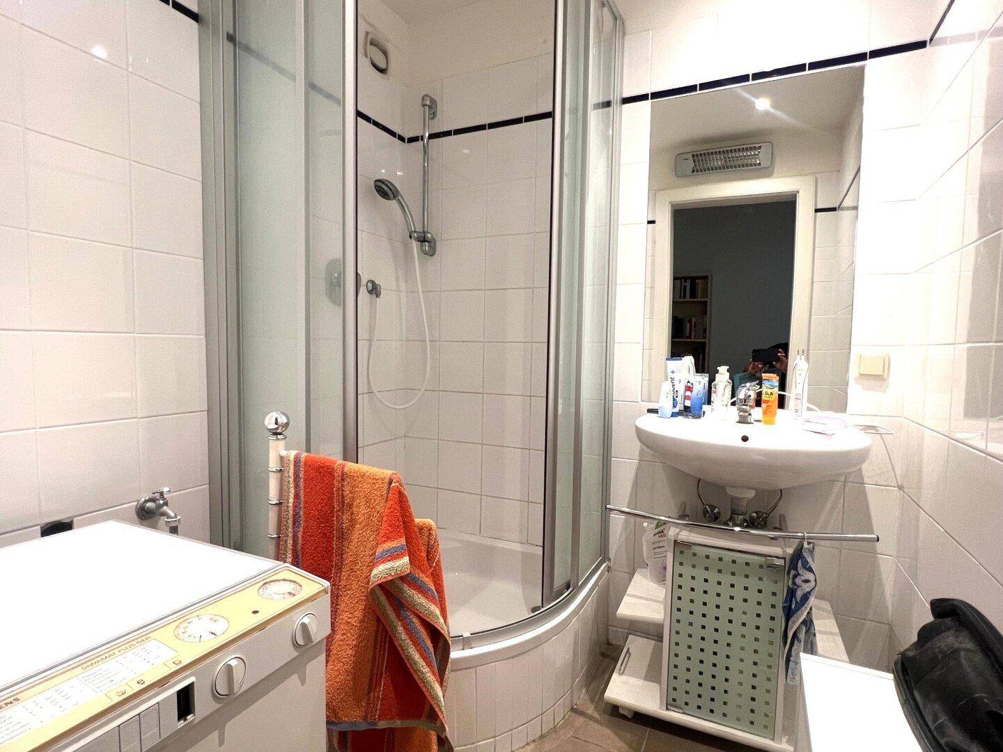 Badezimmer mit Duschkabine, Waschbecken und Waschmaschine.