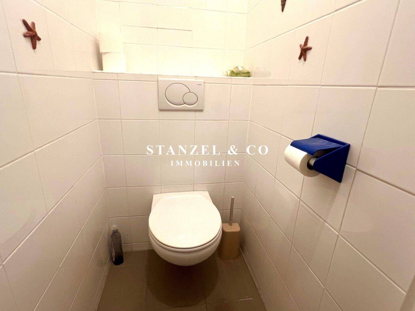 Separates WC mit Wand-WC und weißen Fliesen.