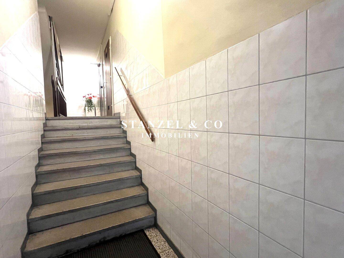 Treppenaufgang mit gefliesten Wänden und Terrazzostufen.