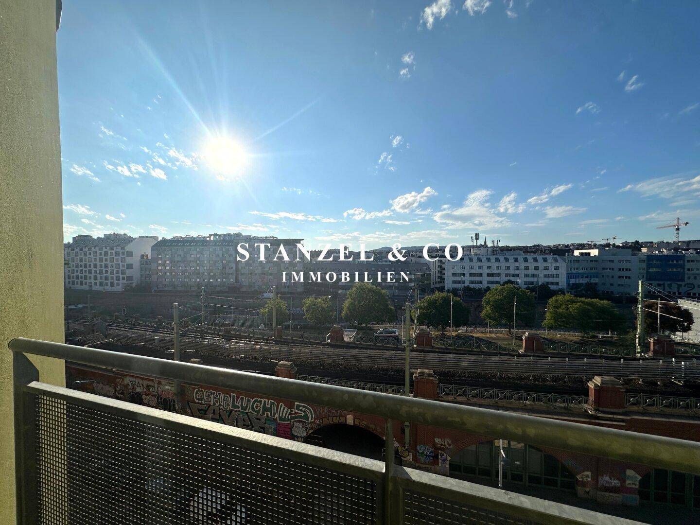 Sonniger Ausblick vom Balkon auf die Bahngleise und die Skyline der Stadt.