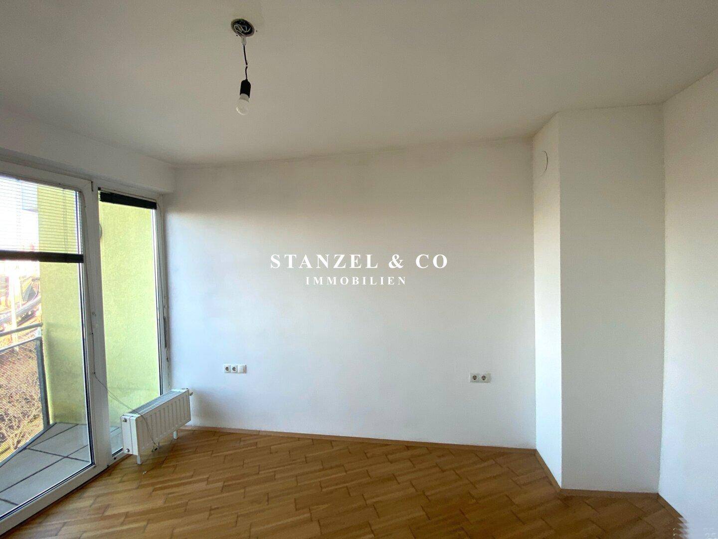 Geräumiges Zimmer mit hellem Parkettboden und großen Fenstern, die viel Tageslicht hereinlassen.