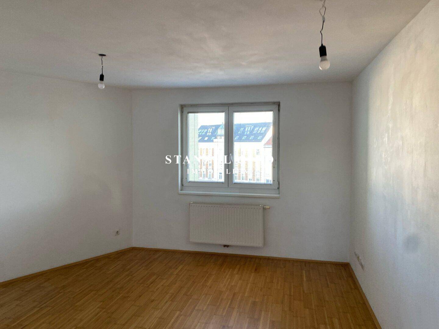 Helles Zimmer mit Parkettboden und einem Fenster, ideal als Schlaf- oder Arbeitszimmer.