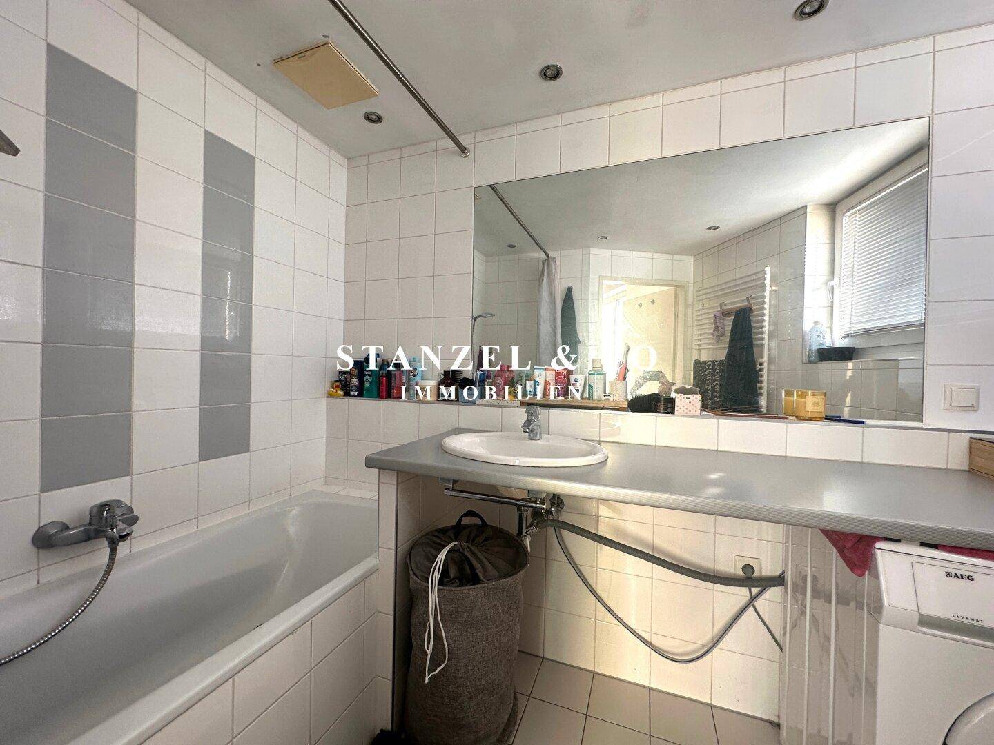 Badezimmer mit Badewanne, Waschbecken, großem Spiegel und integrierter Waschmaschine.