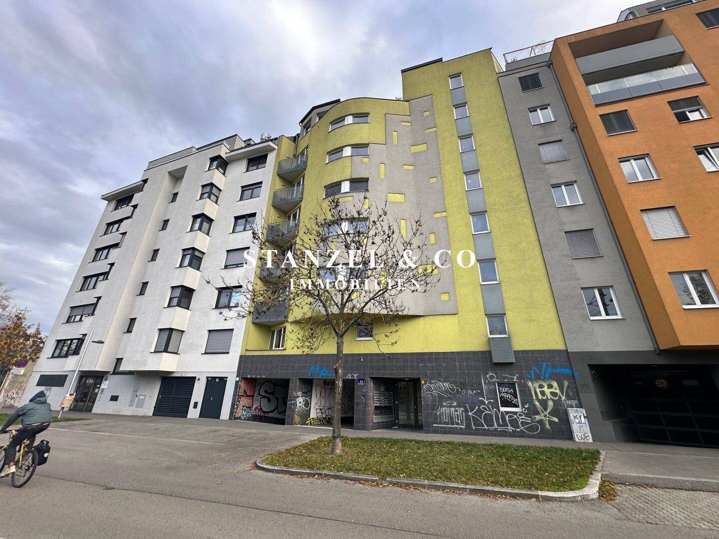 Moderne Wohngebäude-Fassade mit gelben und grauen Elementen sowie Balkonen in urbaner Umgebung.