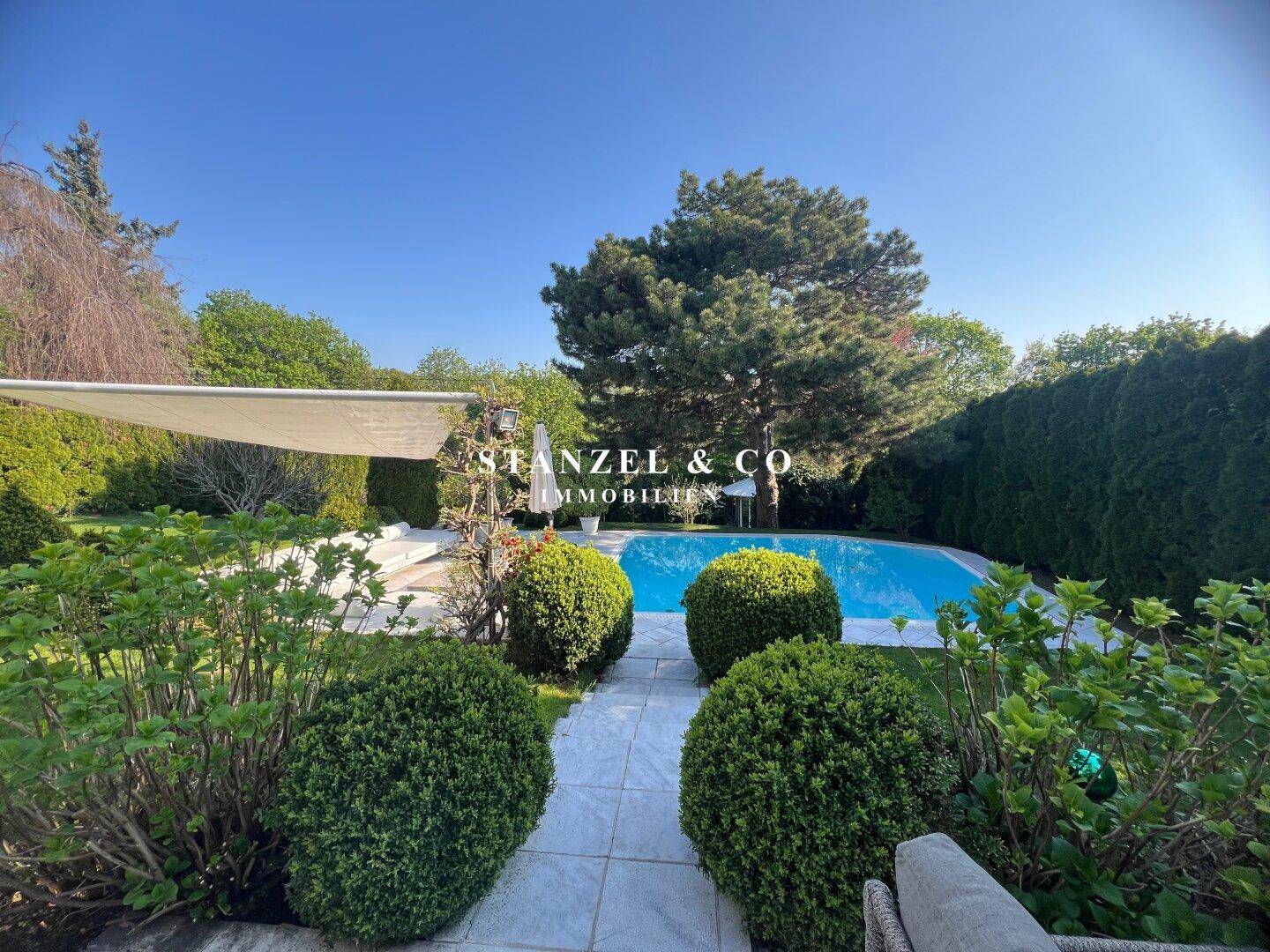 Weitläufiger Garten mit Pool und gepflegten Sträuchern unter strahlend blauem Himmel.