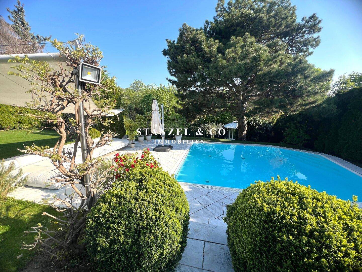 Gepflegter Gartenbereich mit Pool und üppiger Bepflanzung unter strahlend blauem Himmel.