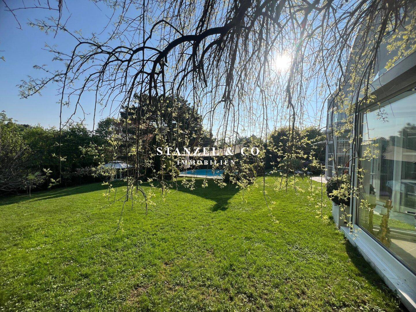 Großer, gepflegter Rasenbereich mit Bäumen und Blick auf den Pool im Hintergrund.