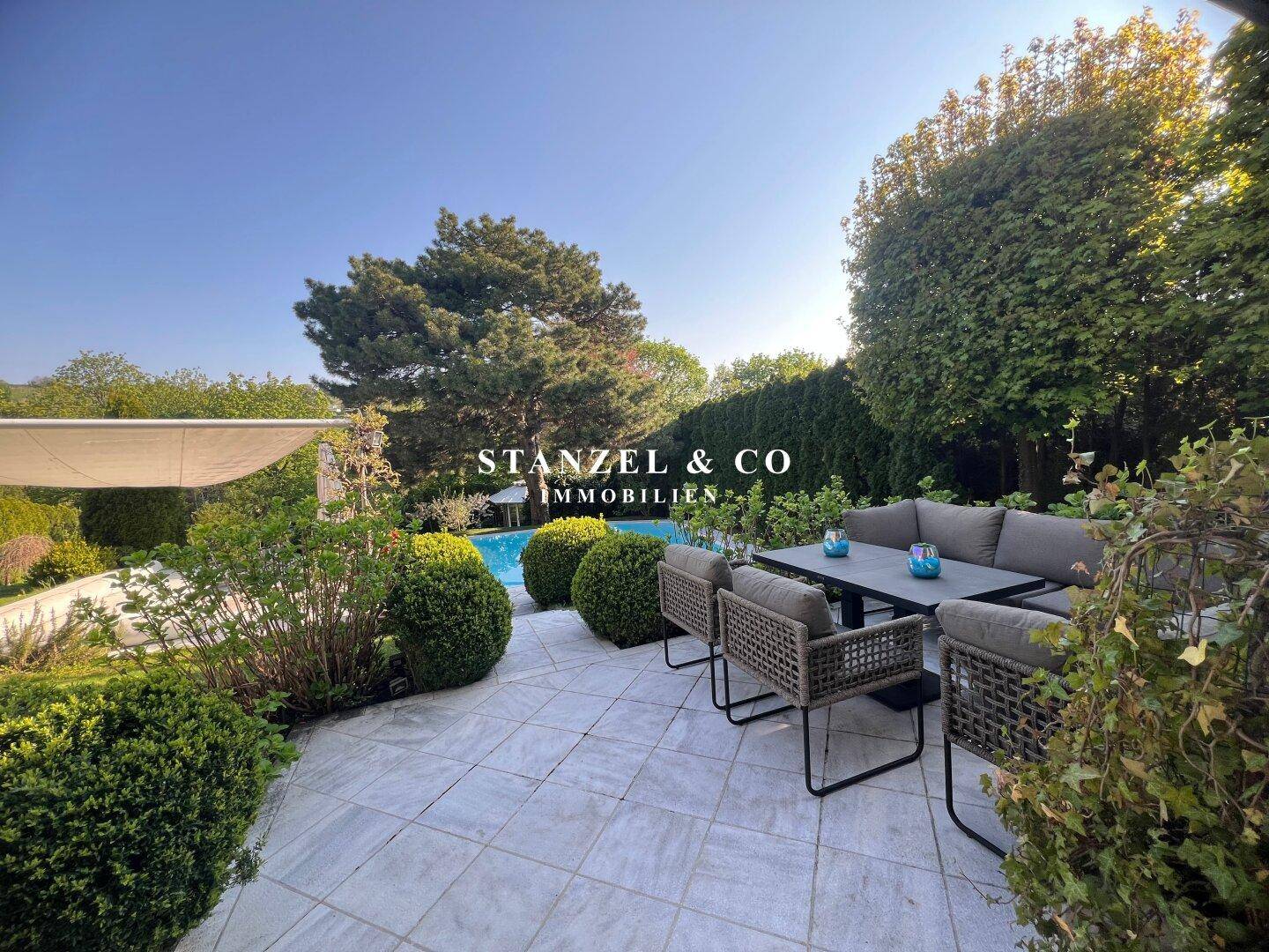 Gemütliche Terrasse mit modernen Gartenmöbeln und Blick auf den Pool und Garten.