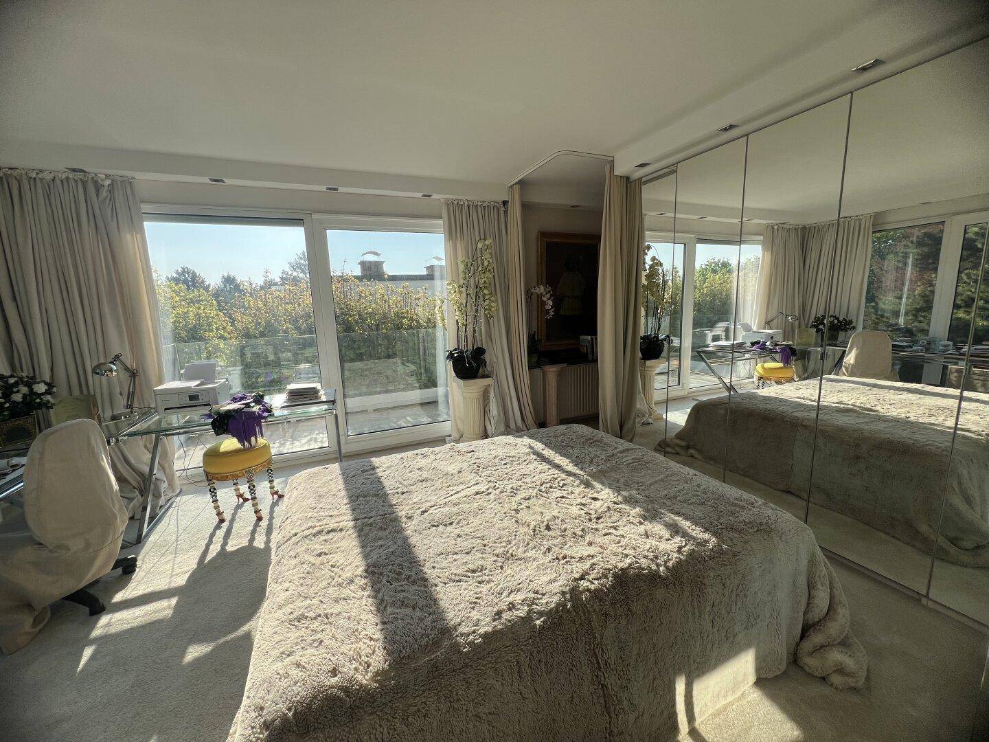 Helles Schlafzimmer mit großen Fenstern, Teppichboden und Spiegelschränken.
