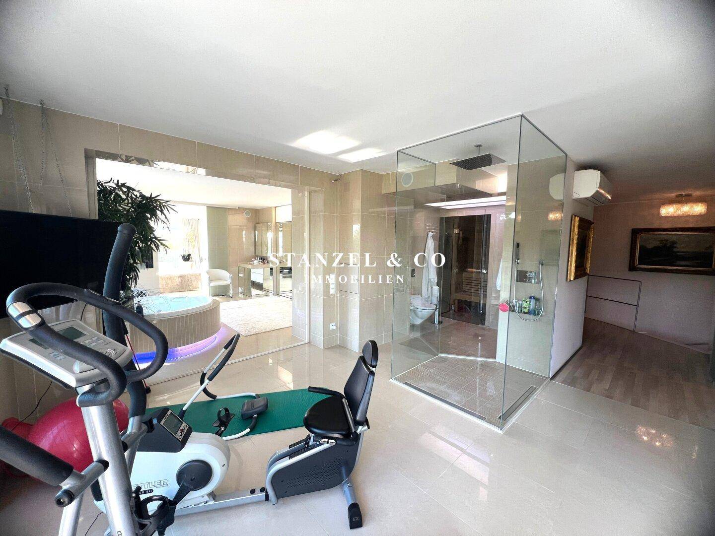Fitnessbereich mit Trainingsgeräten, Blick auf Whirlpool und Sauna, ideal für Wellness und Sport.