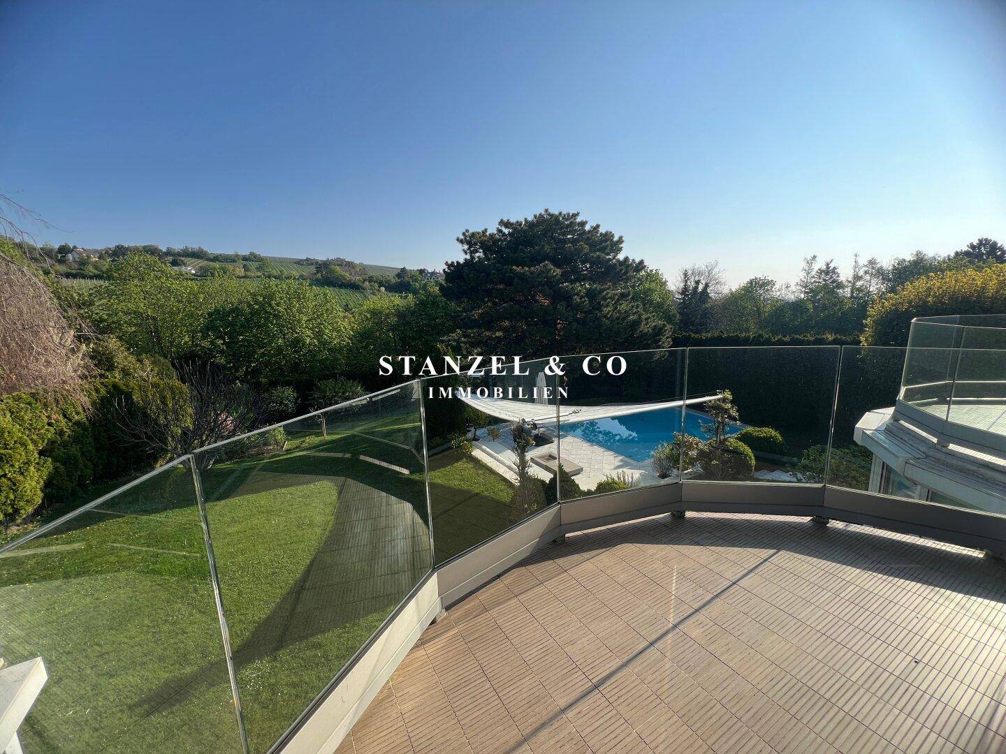 Großer Balkon mit Glasgeländer und weitem Blick über den Garten und die Landschaft.
