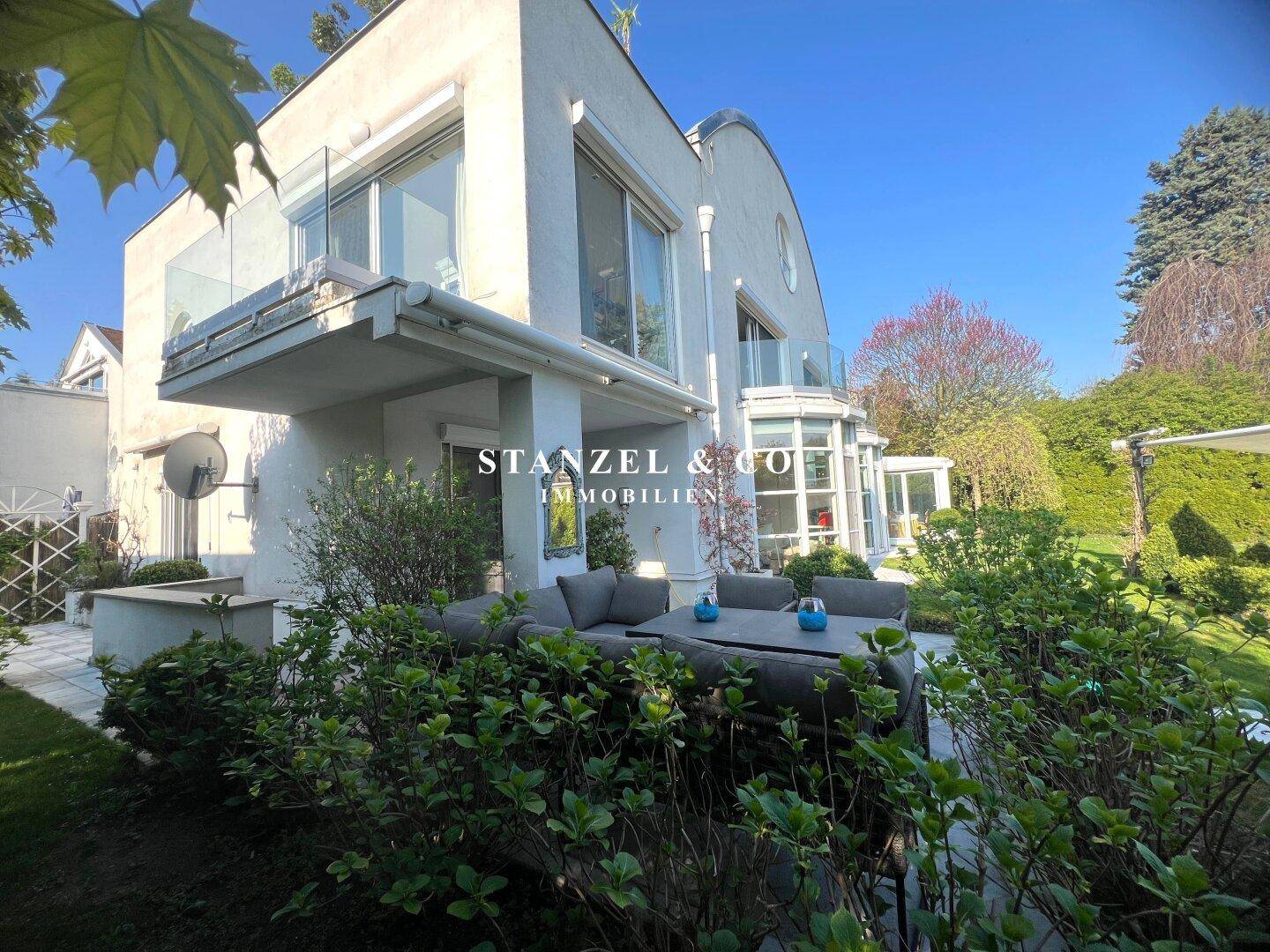 Elegante Hausfassade mit Balkonen, Terrasse und Blick auf den gepflegten Garten.