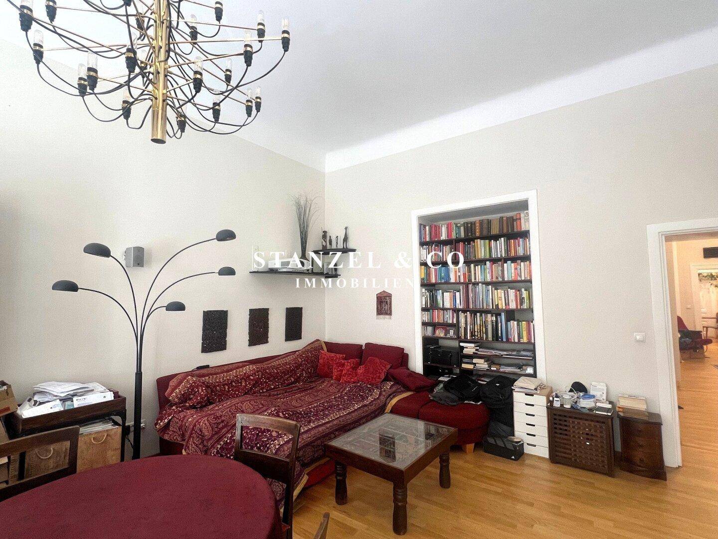 Geräumiges Wohnzimmer mit Kronleuchter, rotem Sofa und integriertem Bücherregal.