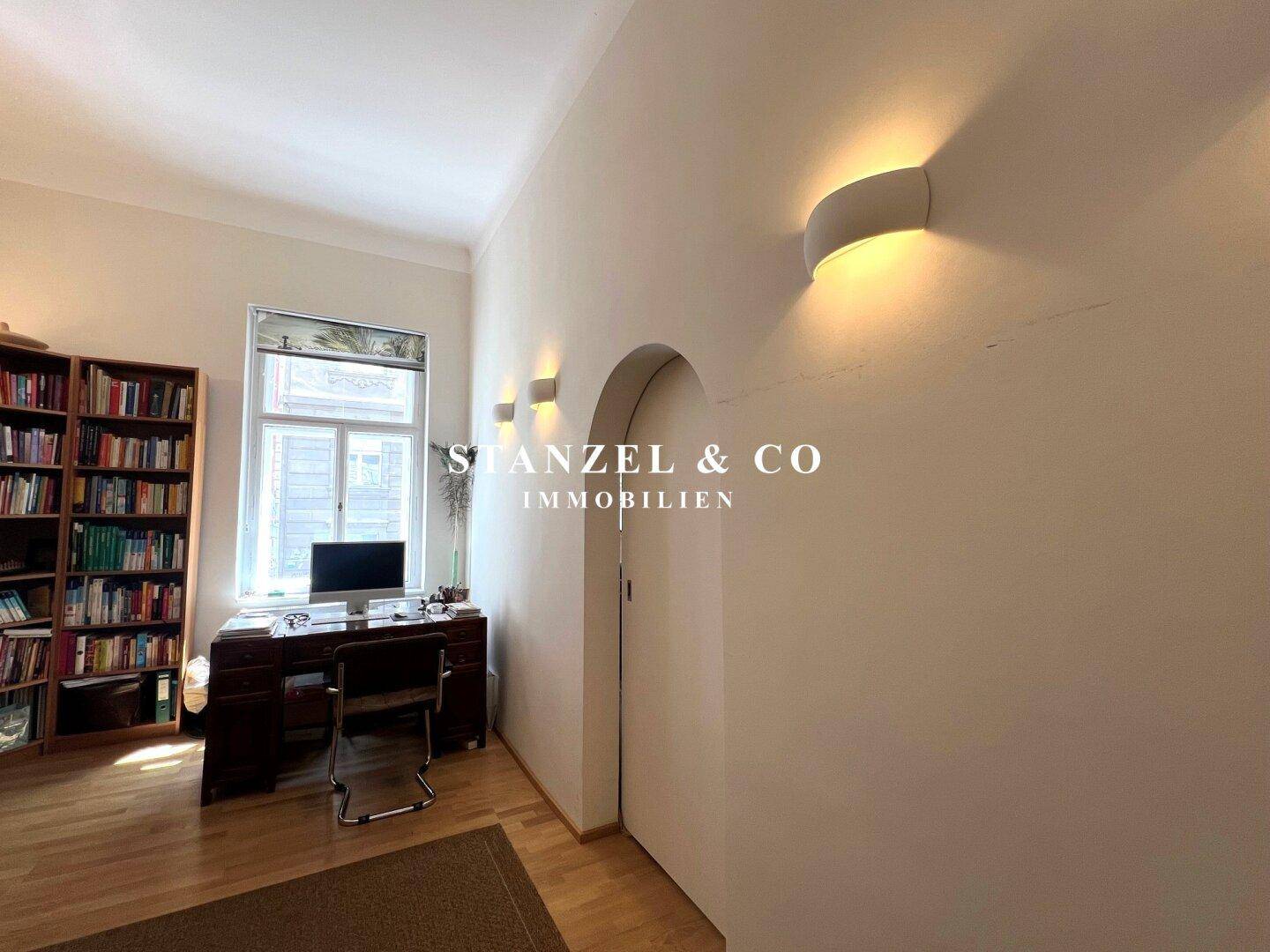 Arbeitszimmer mit großem Schreibtisch, Bücherregal und Wandleuchten.