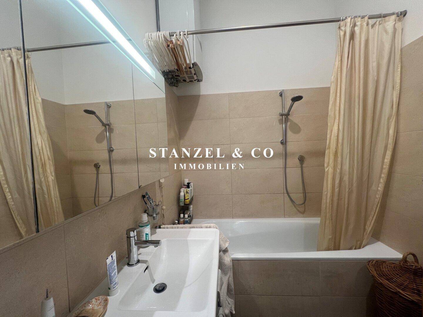 Funktionales Badezimmer mit Badewanne, Duschvorhang und großem Spiegelschrank über dem Waschbecken.