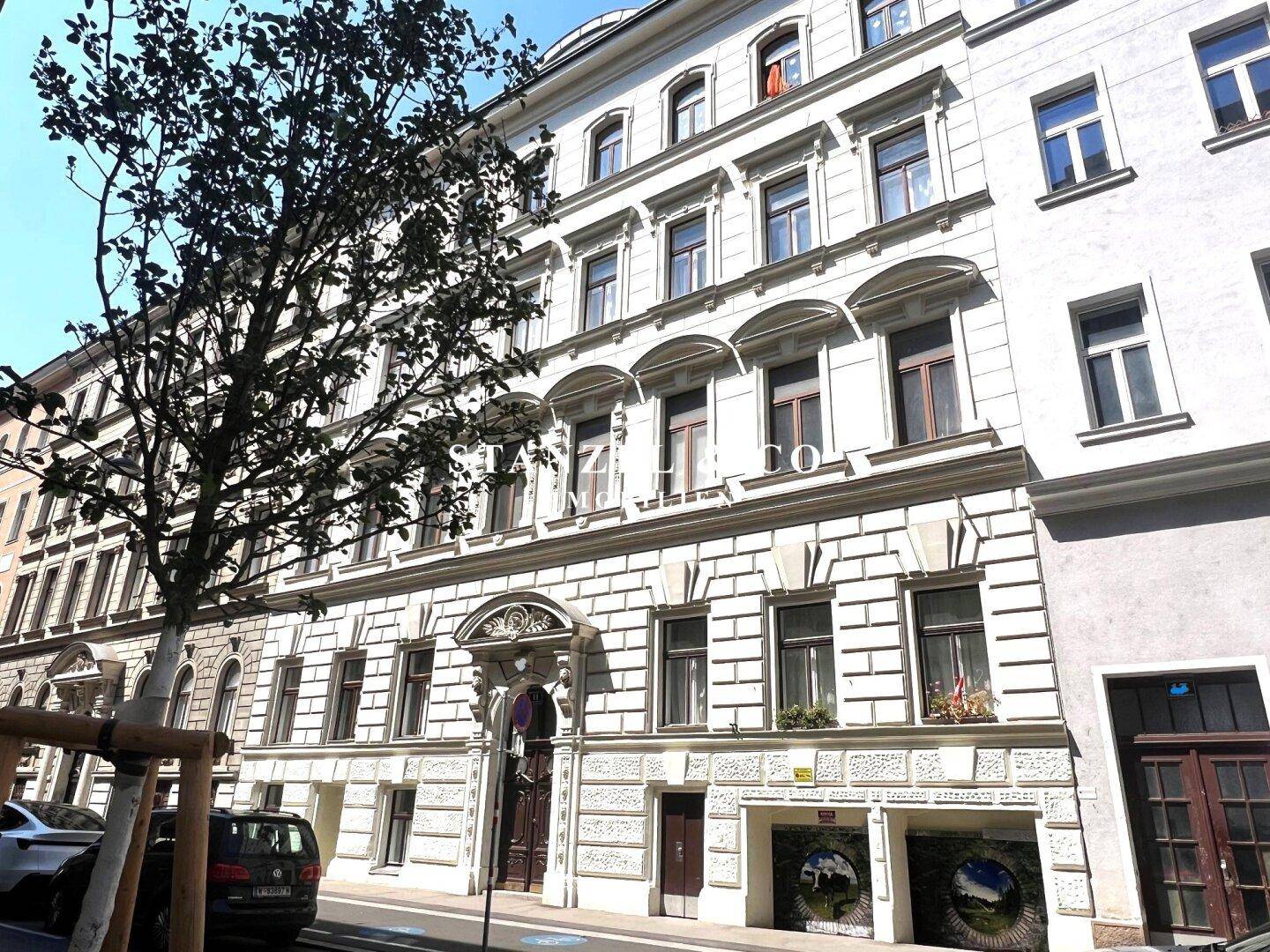 Prächtige Altbaufassade mit detaillierten Verzierungen und großen Fenstern an einem sonnigen Tag.