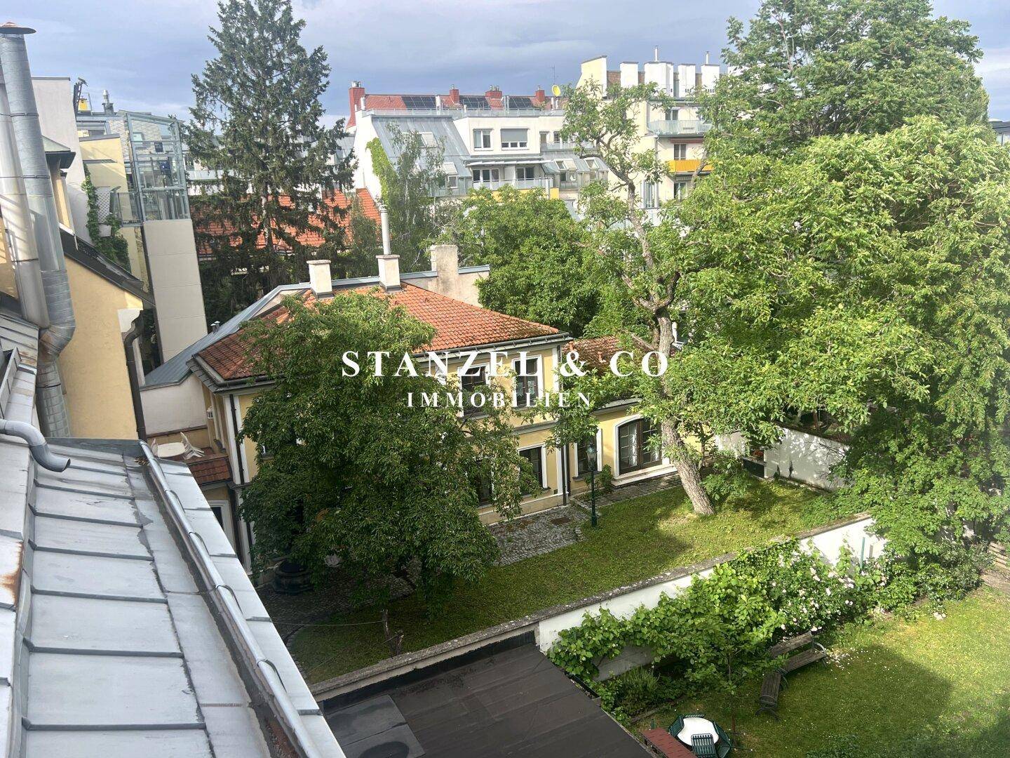 Dachaufsicht auf einen großen Garten mit altem Baumbestand und einem Haus in städtischer Umgebung.