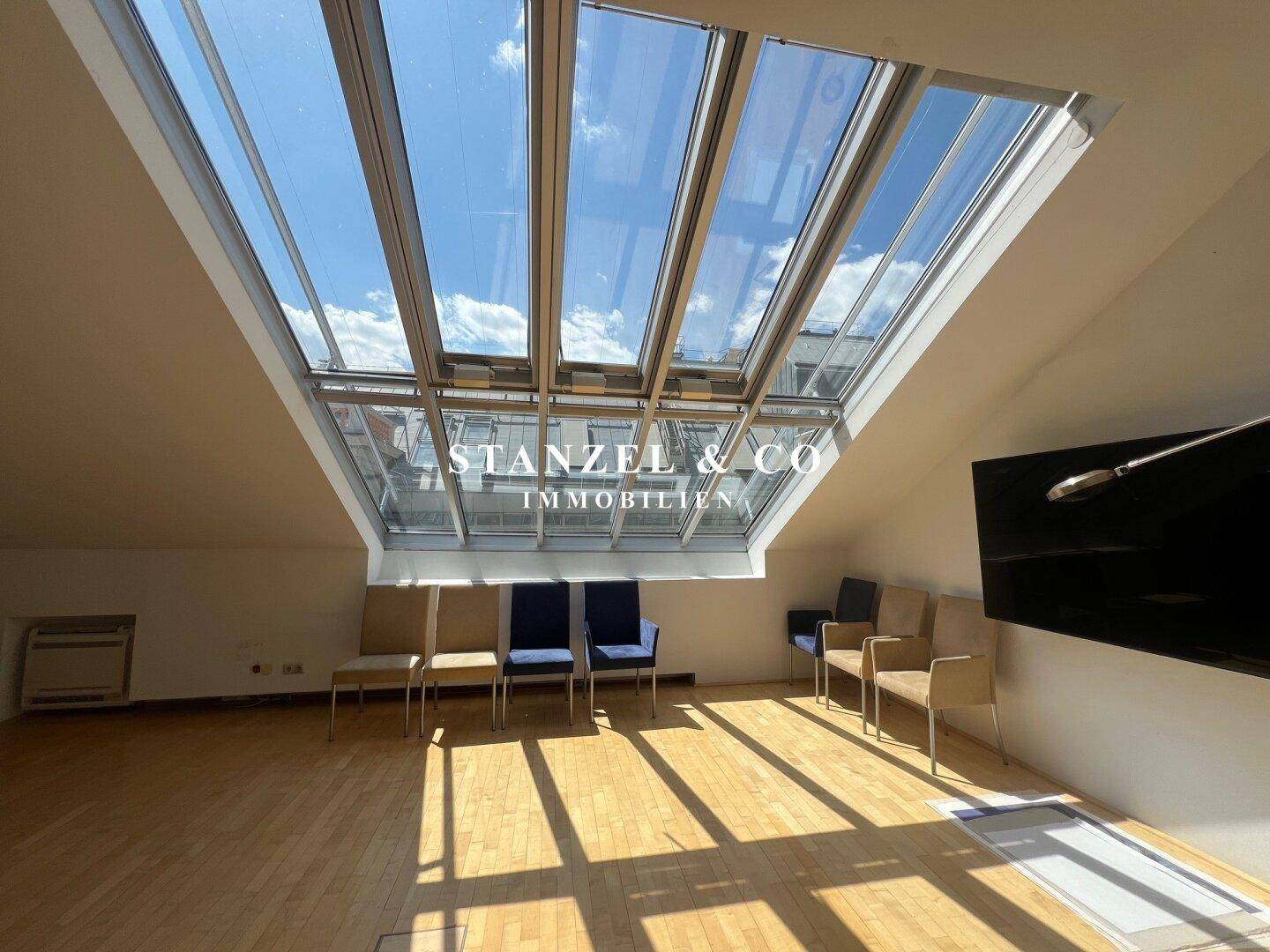 Heller Wohnraum mit Holzboden und großflächigem Glasdach, das den Raum lichtdurchflutet.