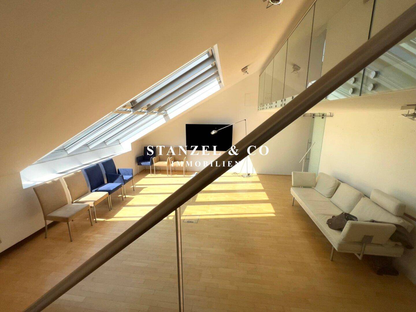 Heller Wohnraum mit Holzboden, moderner Einrichtung und offener Treppe mit Glasgeländer.