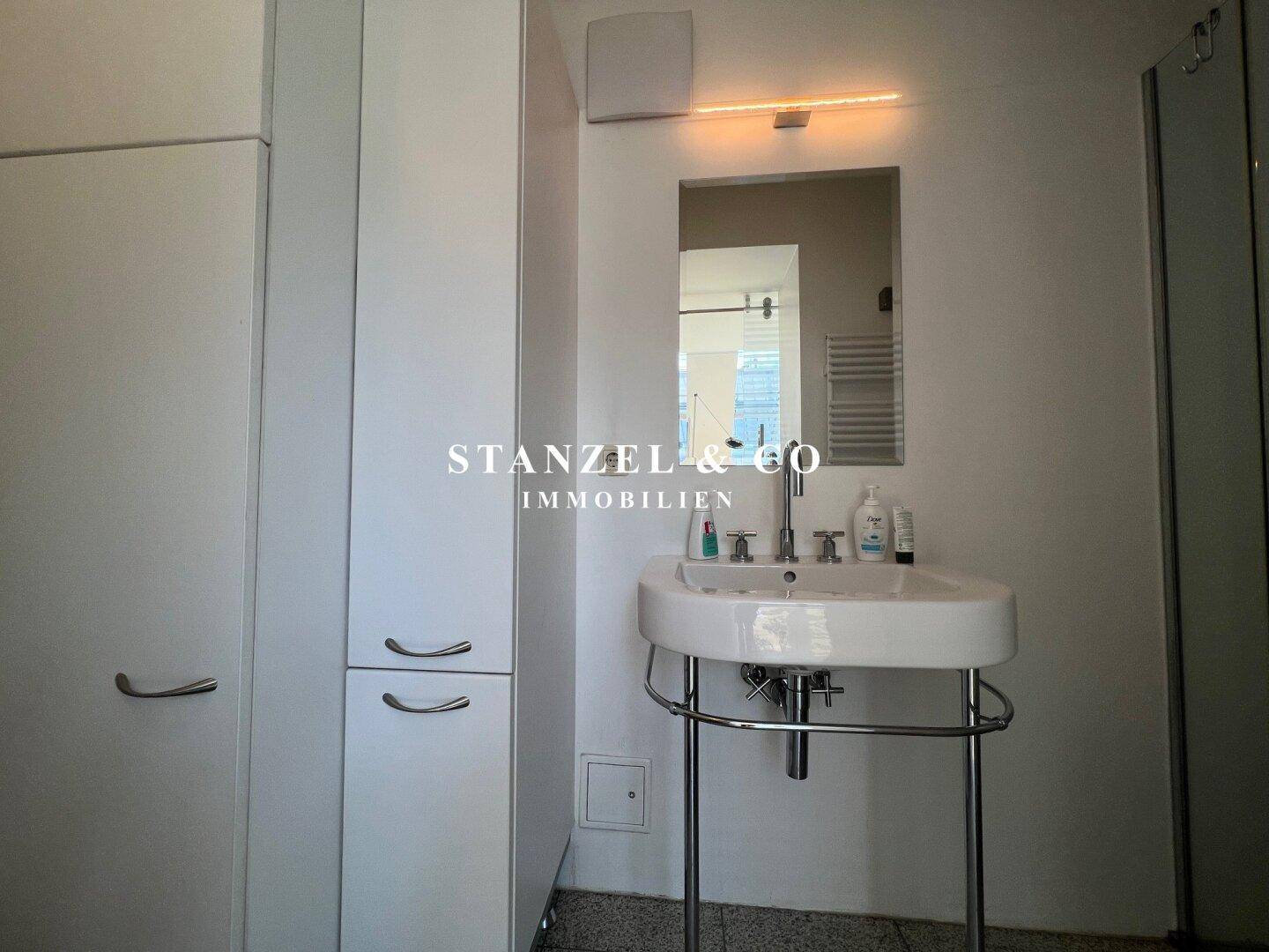 Funktionales Badezimmer mit Waschbecken, Spiegel und praktischen weißen Hochschränken.