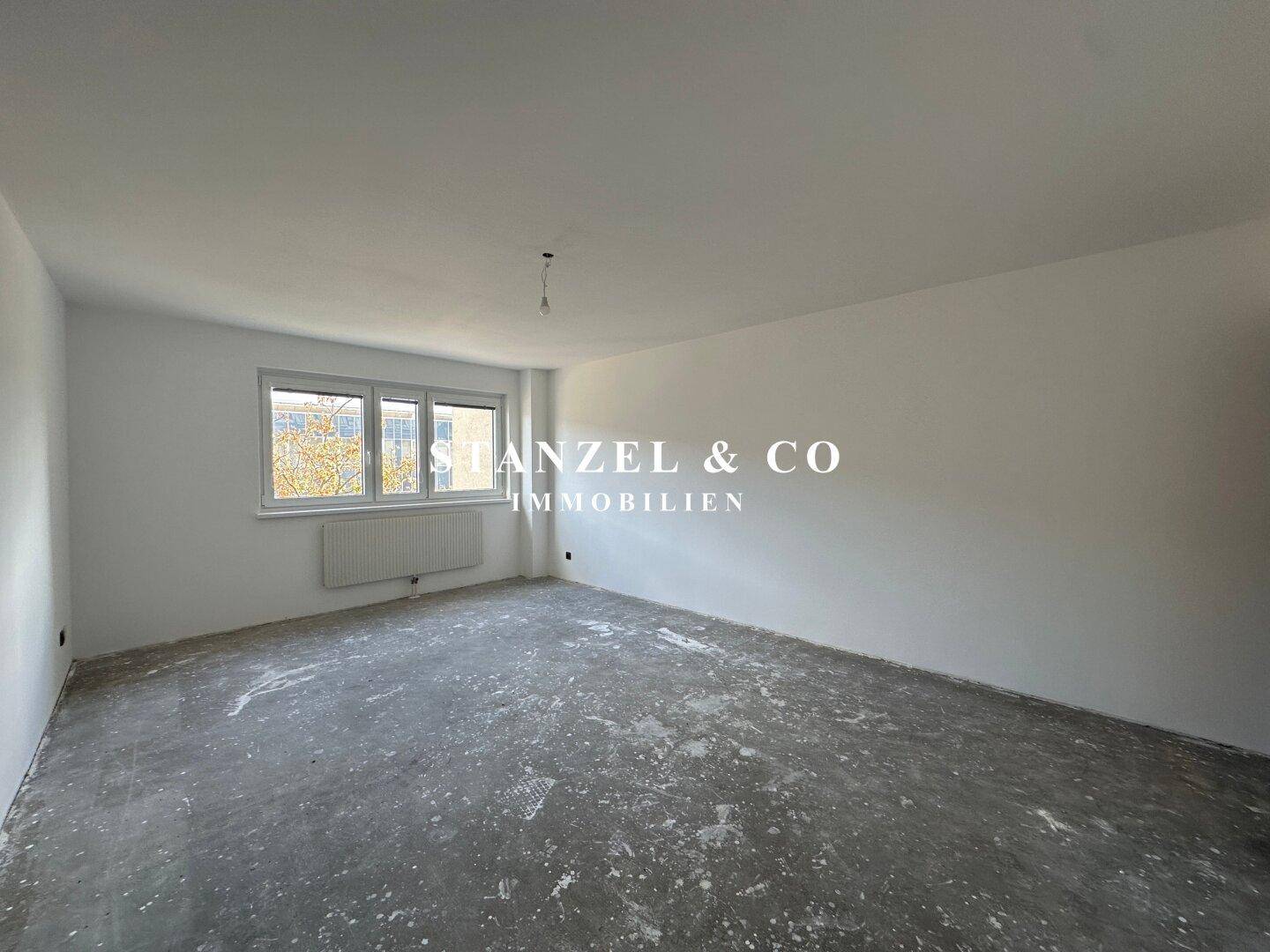 Geräumiger, leerer Raum mit Fensterfront und Rohfußboden, bietet viel Gestaltungspotenzial.