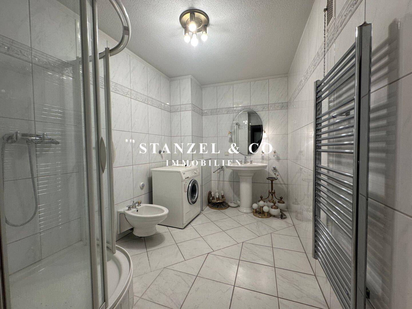 Gefliestes Badezimmer mit Dusche, Bidet, Waschbecken und beheiztem Handtuchhalter.